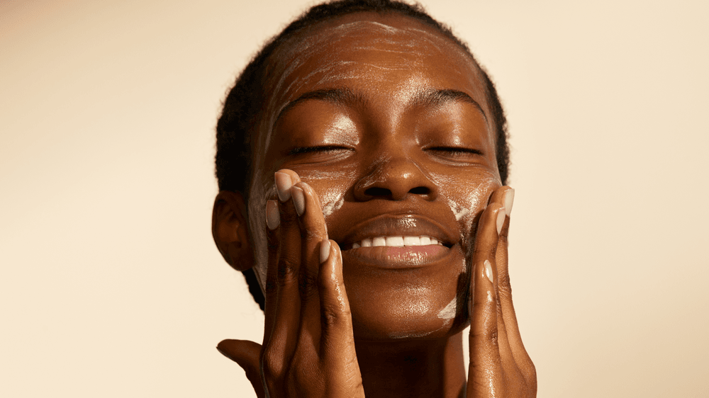 Model smiling as she applies the Oil to Foam Cleanser
