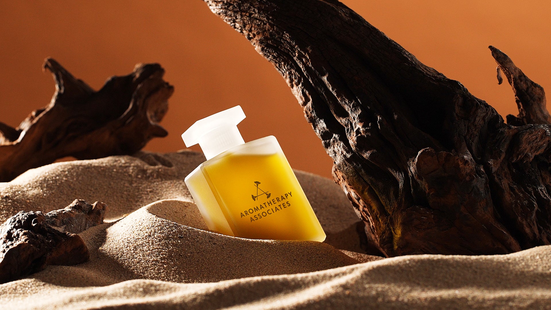 Aromatherapy Associates Desert Therapy bath and shower oil on a sandy surface with driftwood