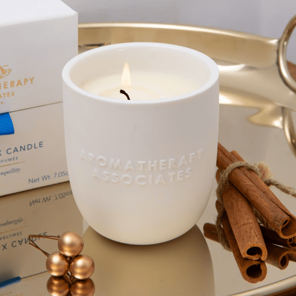 Aromatherapy Associates candle on a reflective surface with cinnamon sticks and a box in the background.