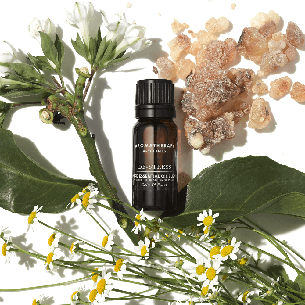 Aromatherapy Associates De-Stress essential oil blend bottle surrounded by flowers and stones on a white background