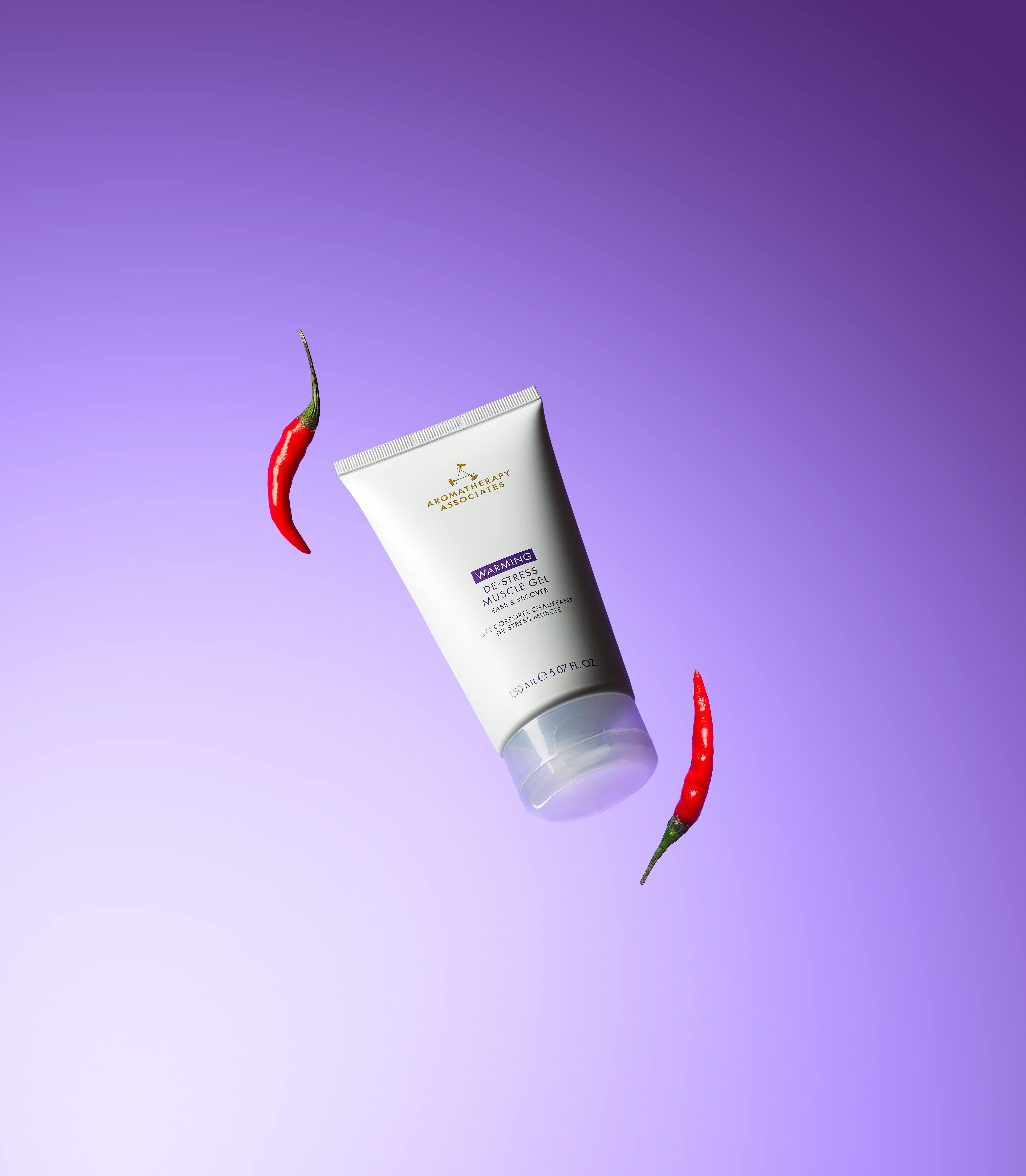 Tube of Warming De-Stress Muscle Gel with red chili peppers on a purple background