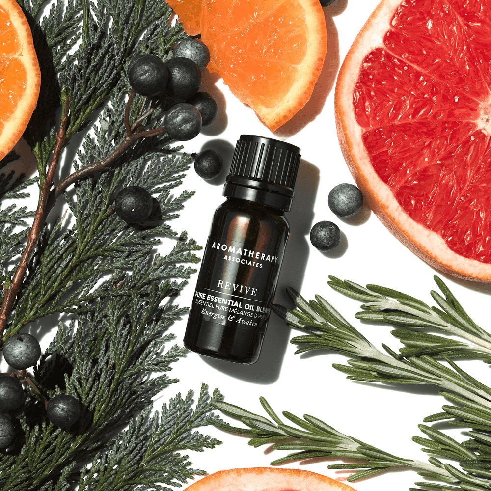 Aromatherapy Associates essential oil blend bottle surrounded by fruits and herbs on a white background