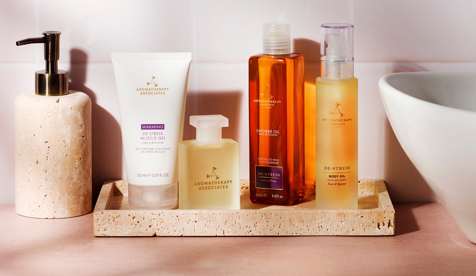 Collection of bath products including a pump bottle, cream, and bottles on a stone tray with a bathroom setting.