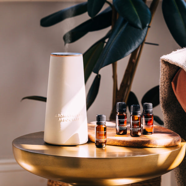 Aromatherapy diffuser and essential oil bottles on a wooden table with plants in the background.