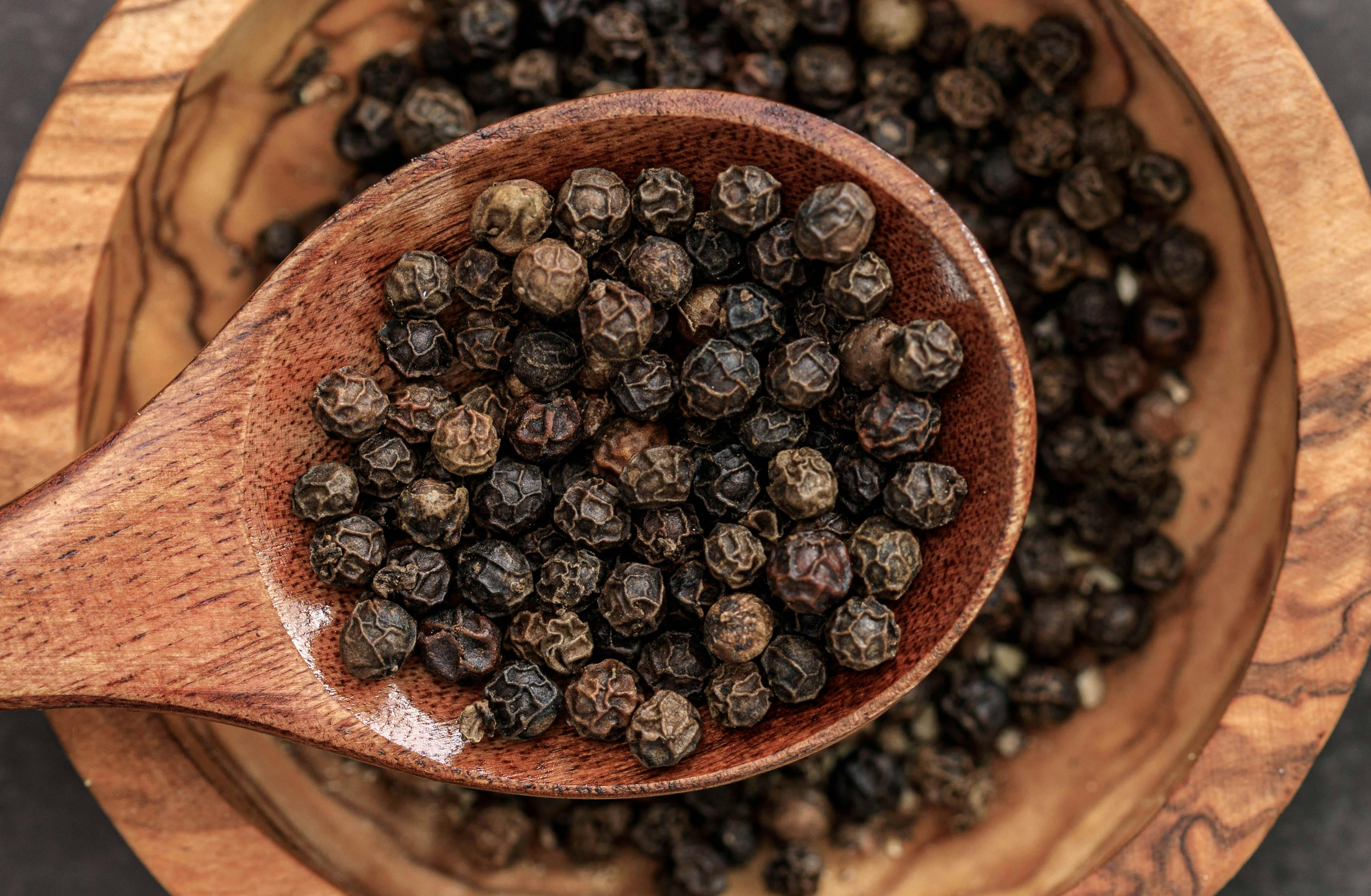 Wooden spoon filled with black peppercorns on a wooden surface